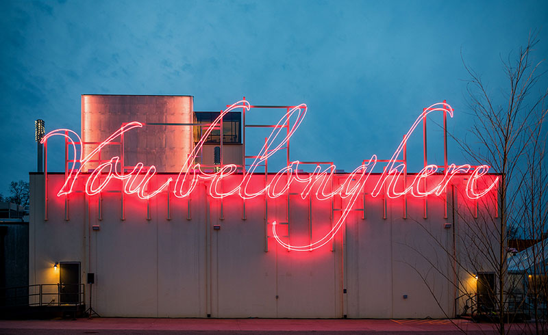 Red neon sign saying You Belong Here on the side of a building