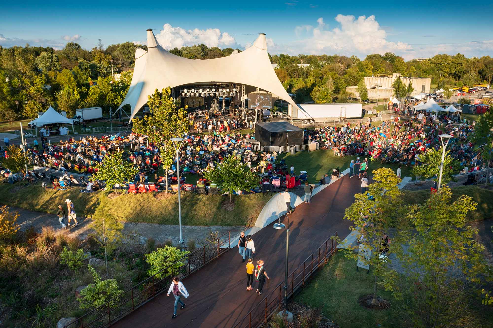 an aerial view of the momentary green as people sit on the lawn and watch a concert from the canopy and walk around