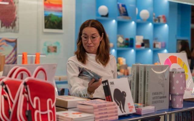 A woman in a white sweater examines a book in the Momentary Shop.