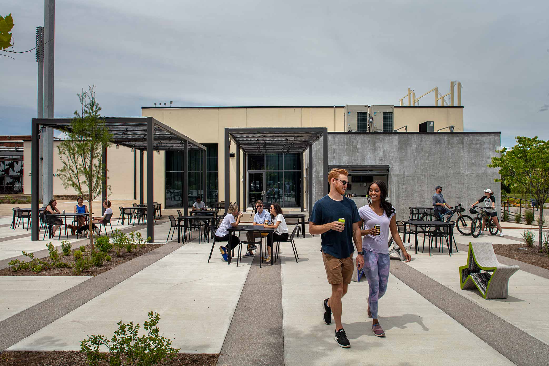 Courtyard area with groups of people at tables with beverages man and women with beverages walks toward foreground