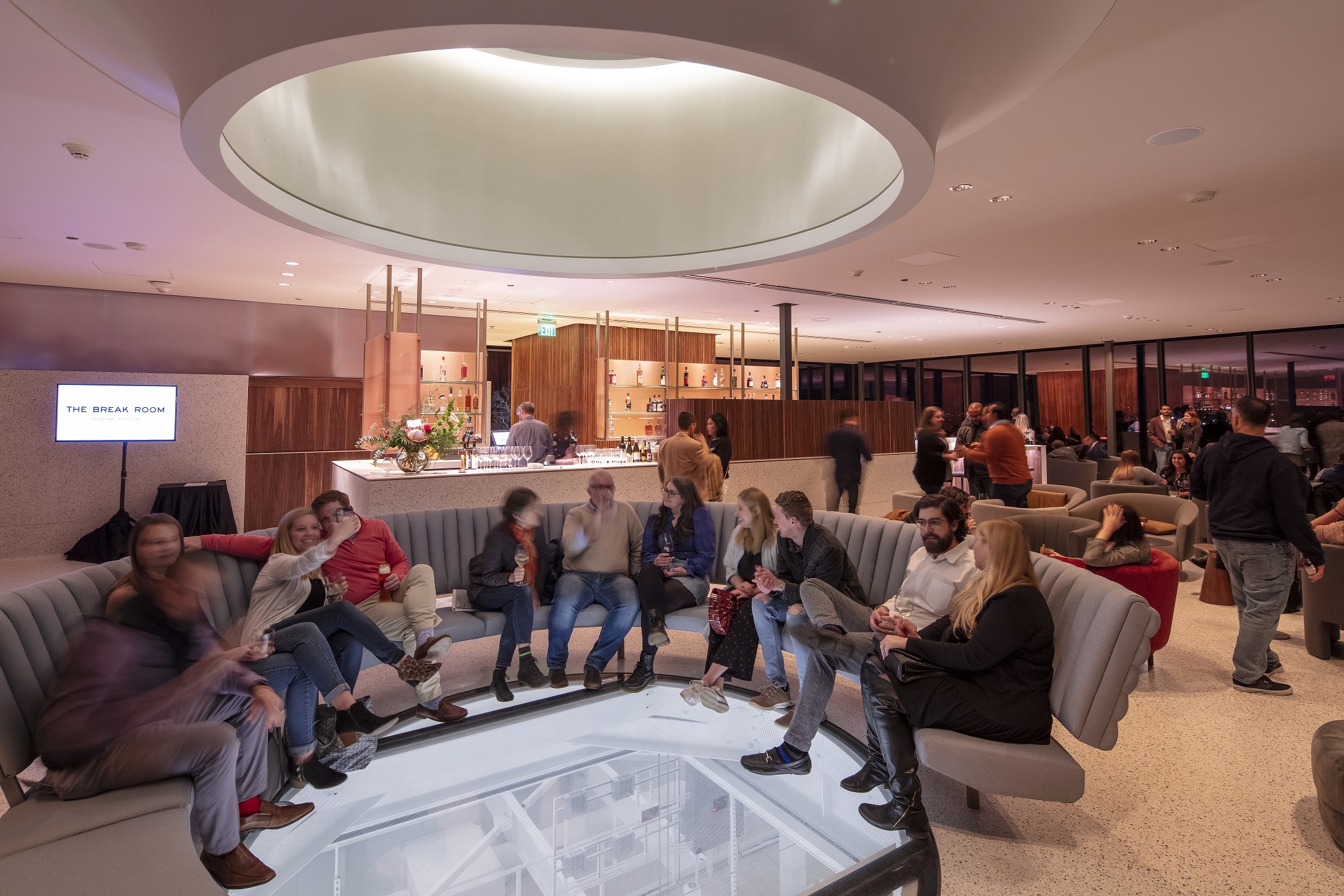 Crowded bar with several people sitting on a circular couch surrounding a glass see through floor