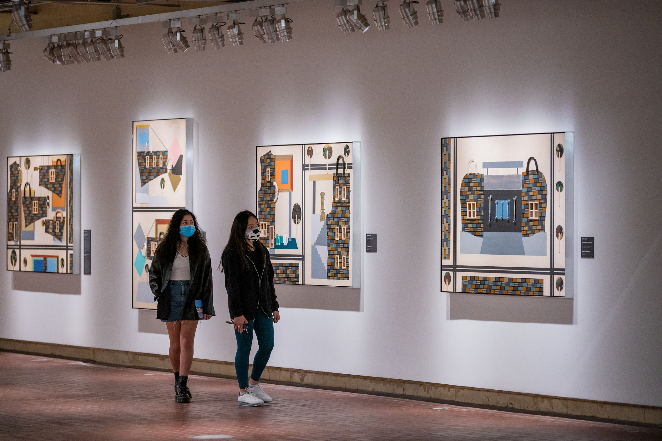 Two young girls walk through the galleries and look at works of collage on the wall