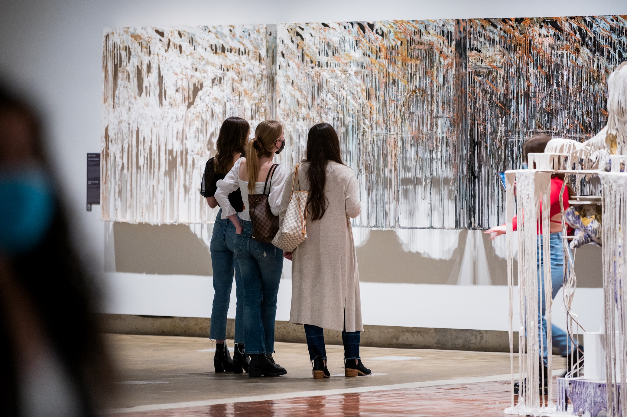 Three young women looking at a white and brown work of art on the wall
