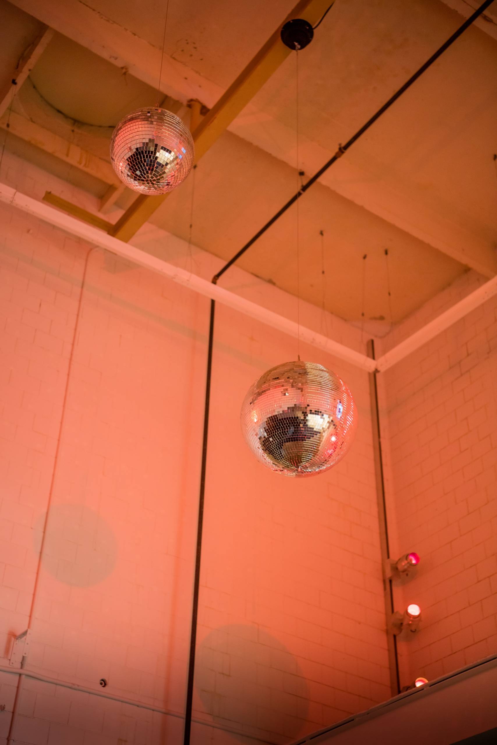 Two disco balls hanging from the ceiling and lit in a pink glow