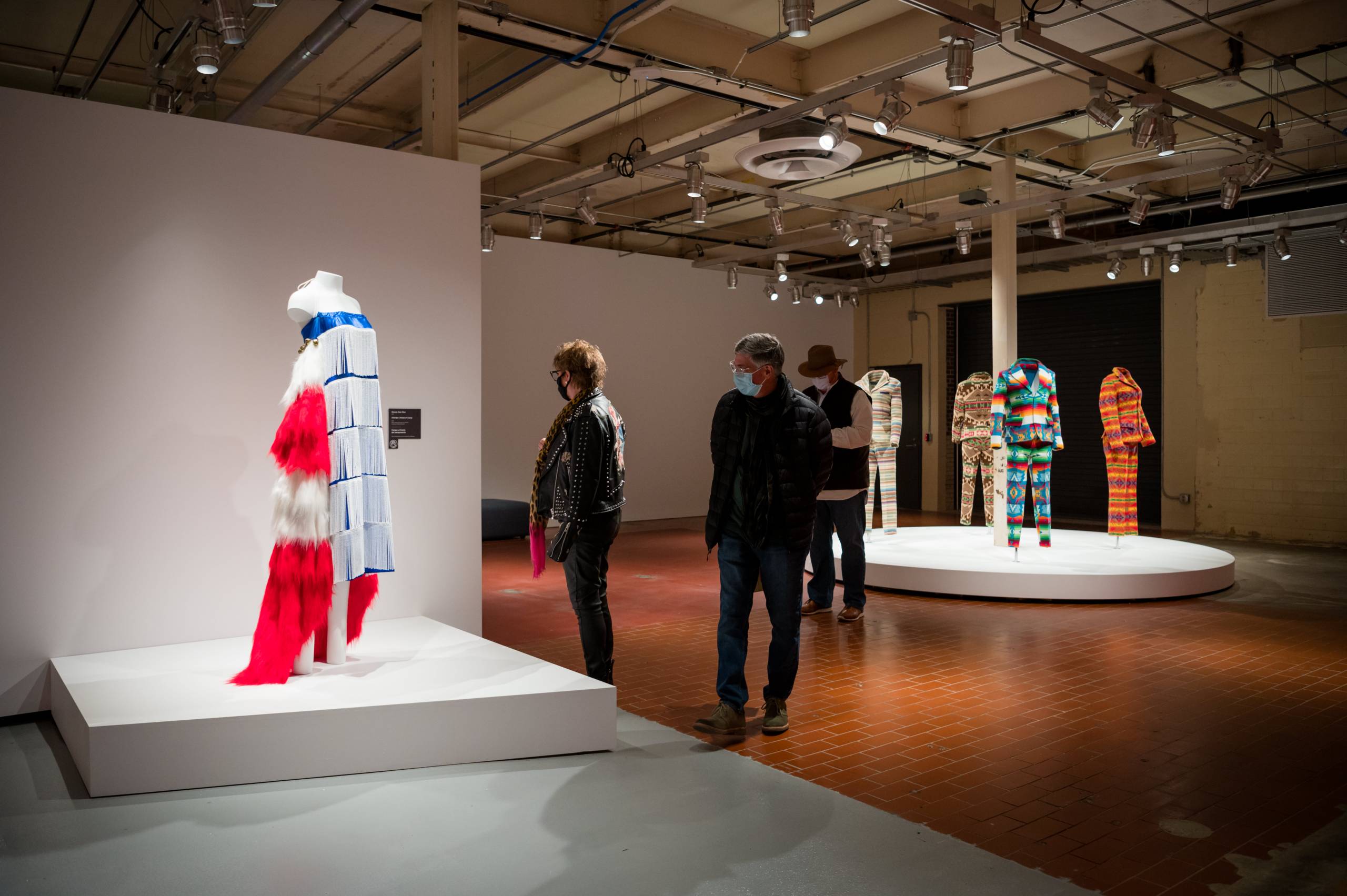 People walking through the galleries and looking at colorful dresses and suits on pedestals