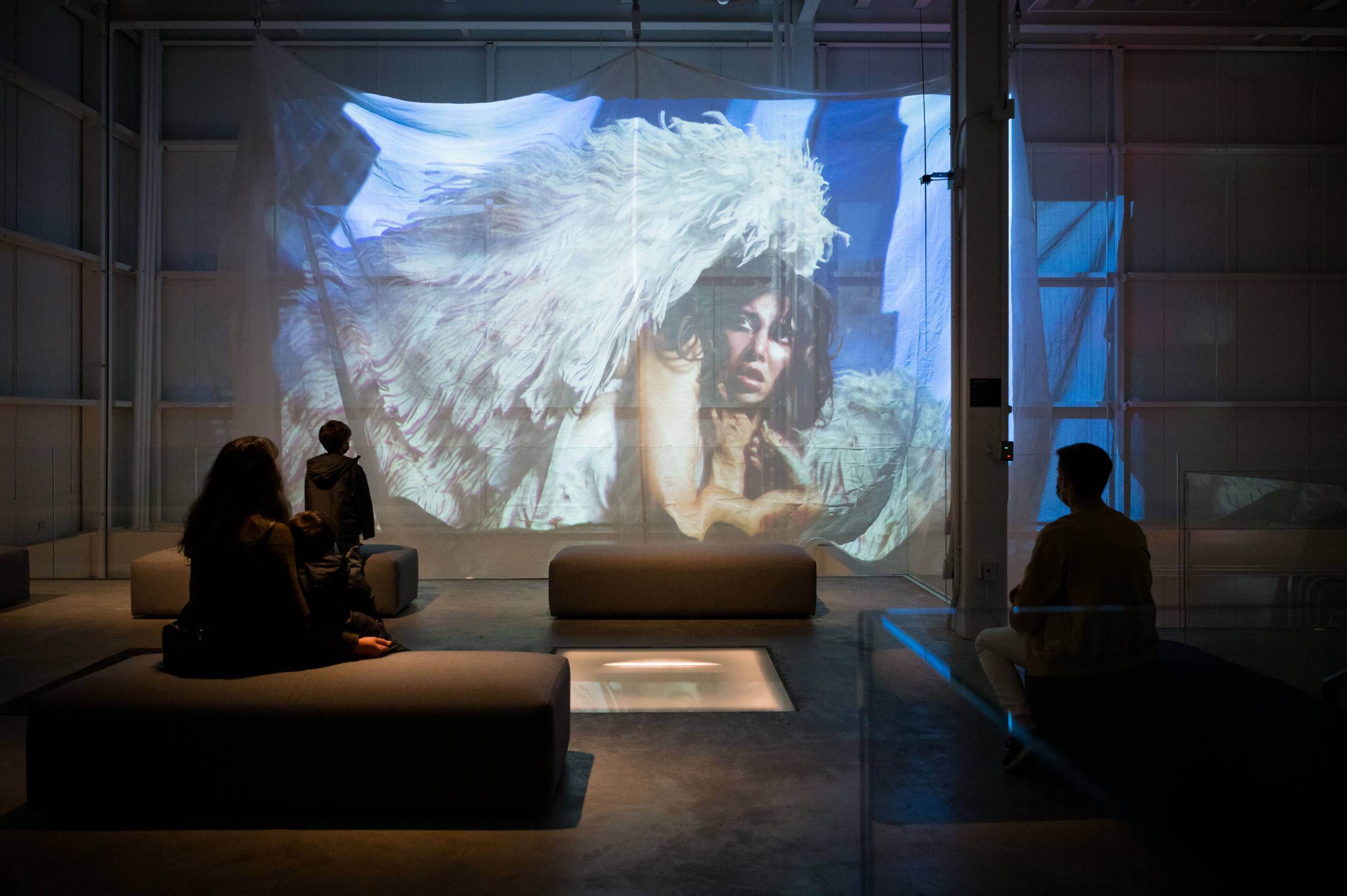 Three figures watching a video of a person wearing angel wings and looking upward