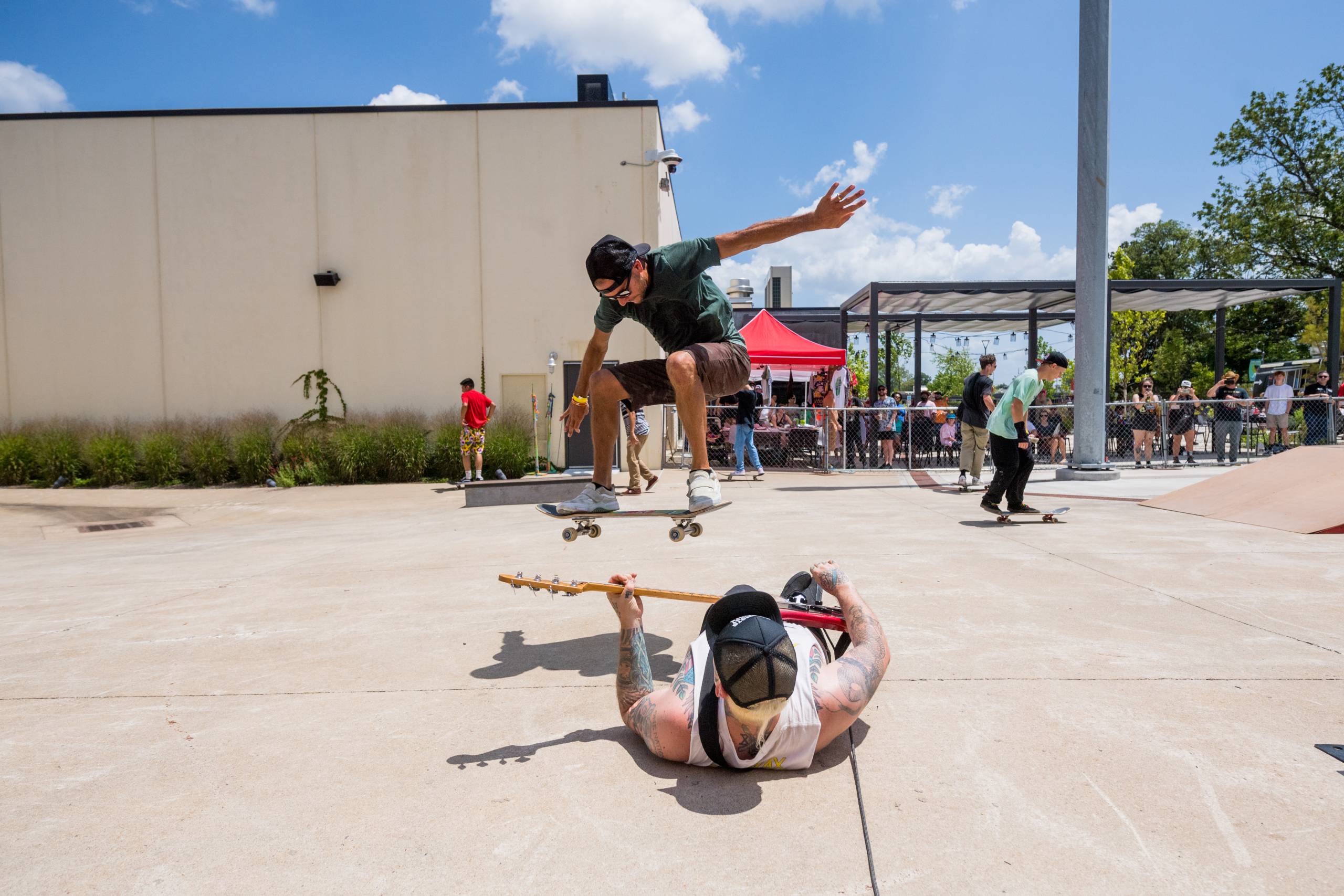 a man on a skateboard jumps over a man with a guitar laying on the ground