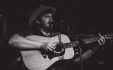 Black and white image of man playing a guitar singing into a microphone