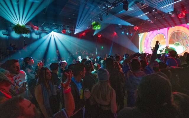 Indoor concert with colorful lights, vibrant crowd dancing and enjoying energetic music.