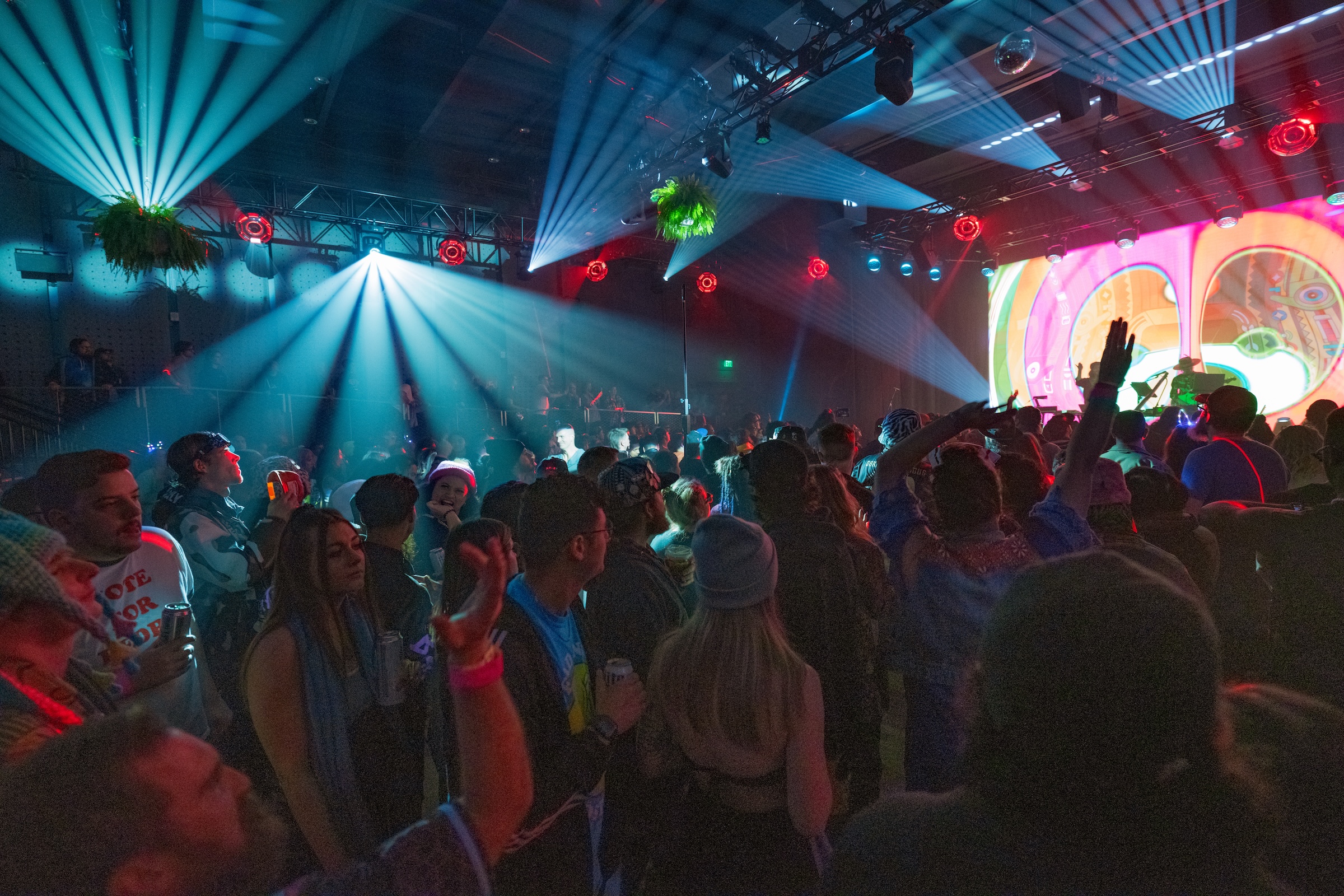 Indoor concert with colorful lights, vibrant crowd dancing and enjoying energetic music.