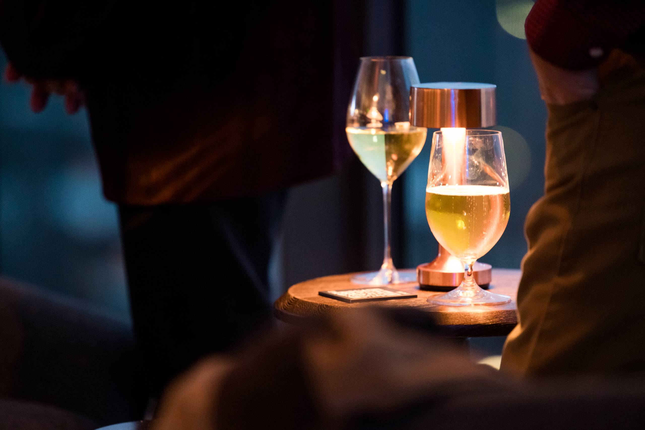 a glass of white wine and a glass of beer on a stand illuminated by a copper desk lamp