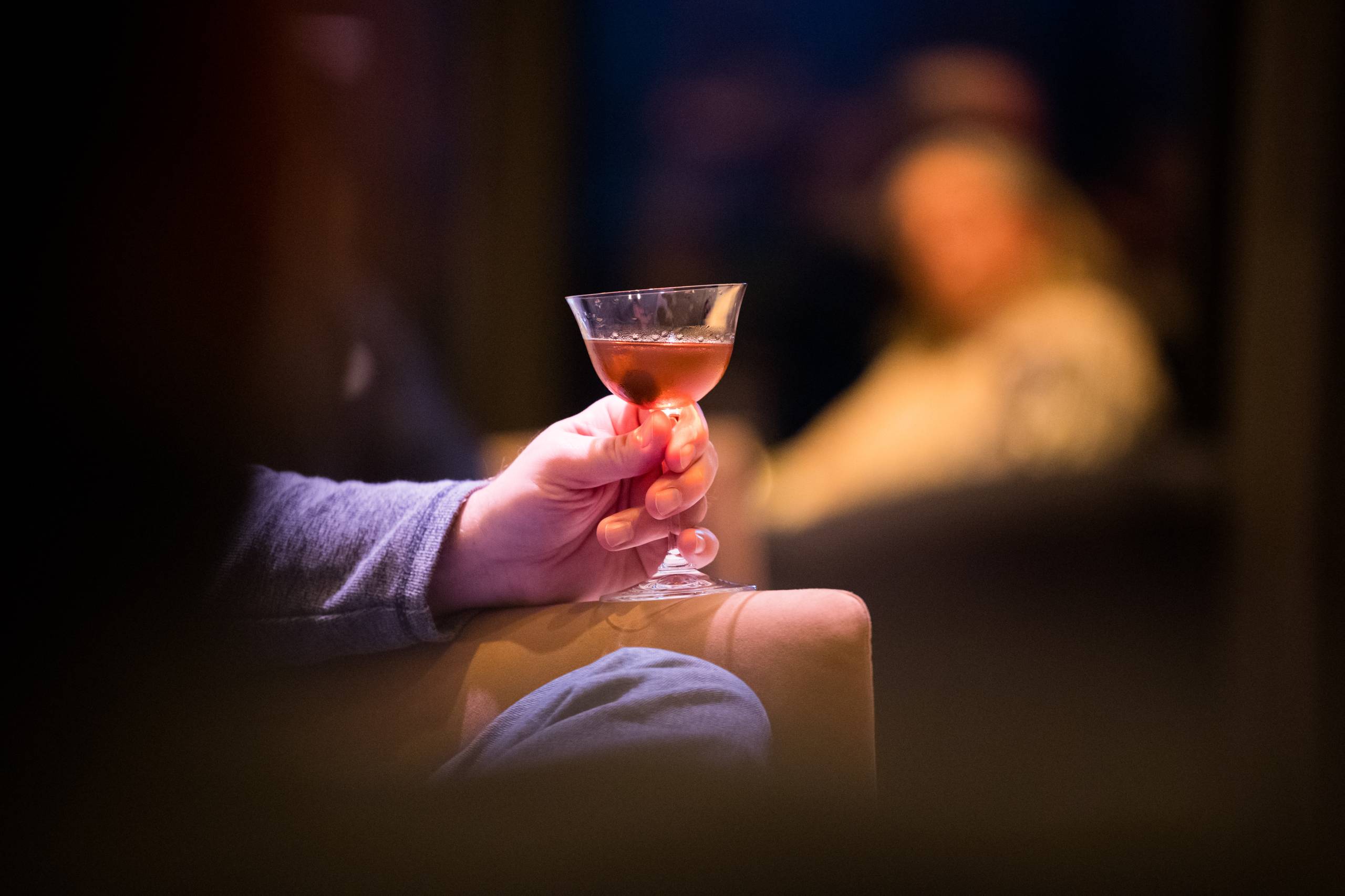 a hand holding a cocktail glass filled with a pink drink and cherry