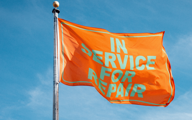 An orange flag waving in the wind, with the words IN SERVICE FOR REPAIR printed in large block letters on the flag.