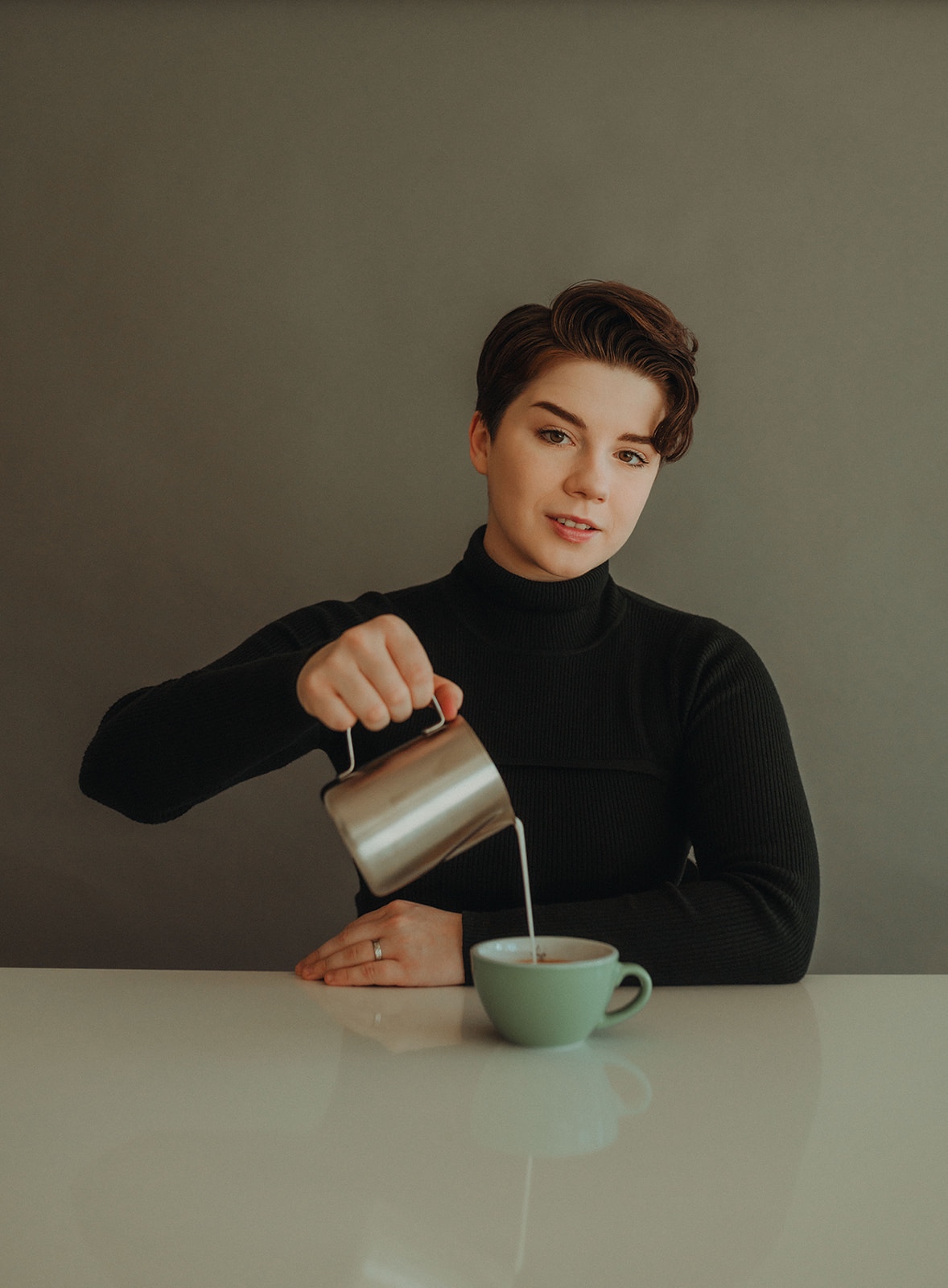 Woman sitting at table pours coffee from a pot into a cup