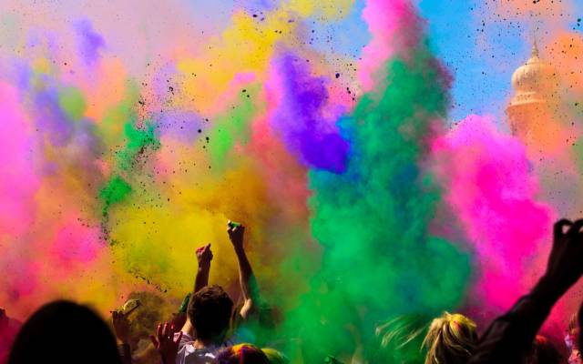 Clouds of colorful pigment powder drift over a cheering crowd as part of Holi celebrations.