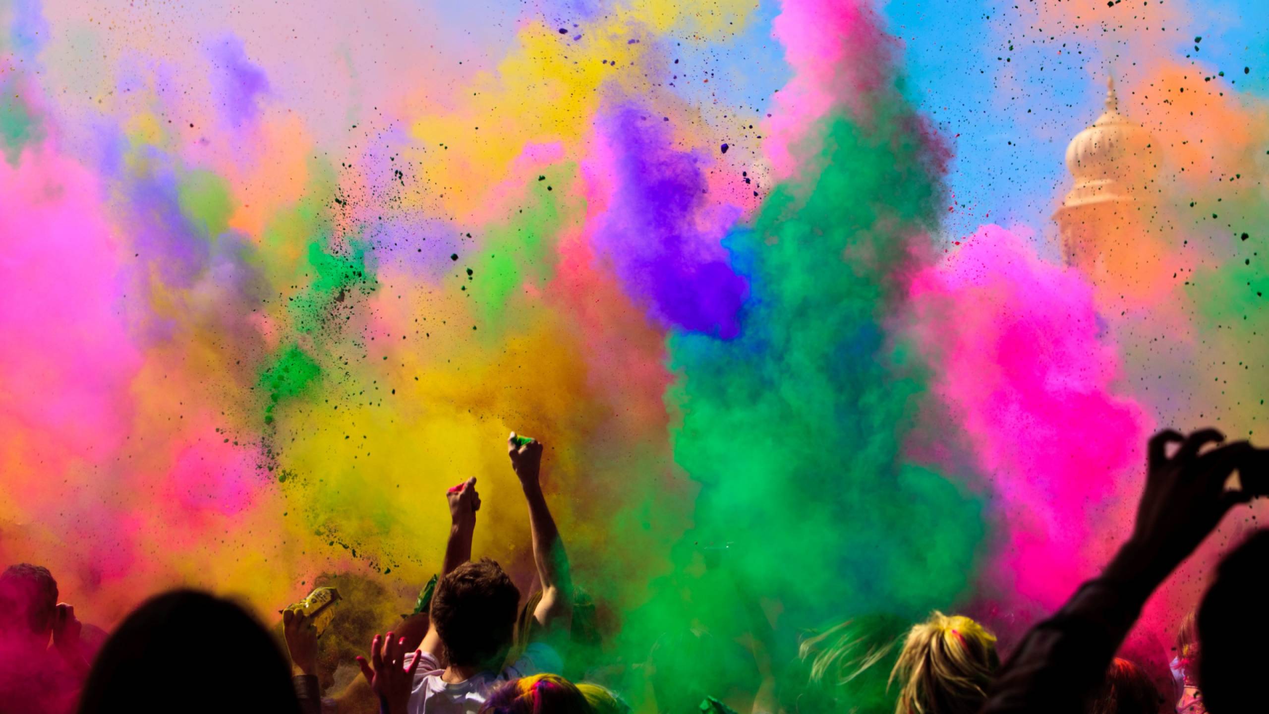 Clouds of colorful pigment powder drift over a cheering crowd as part of Holi celebrations.