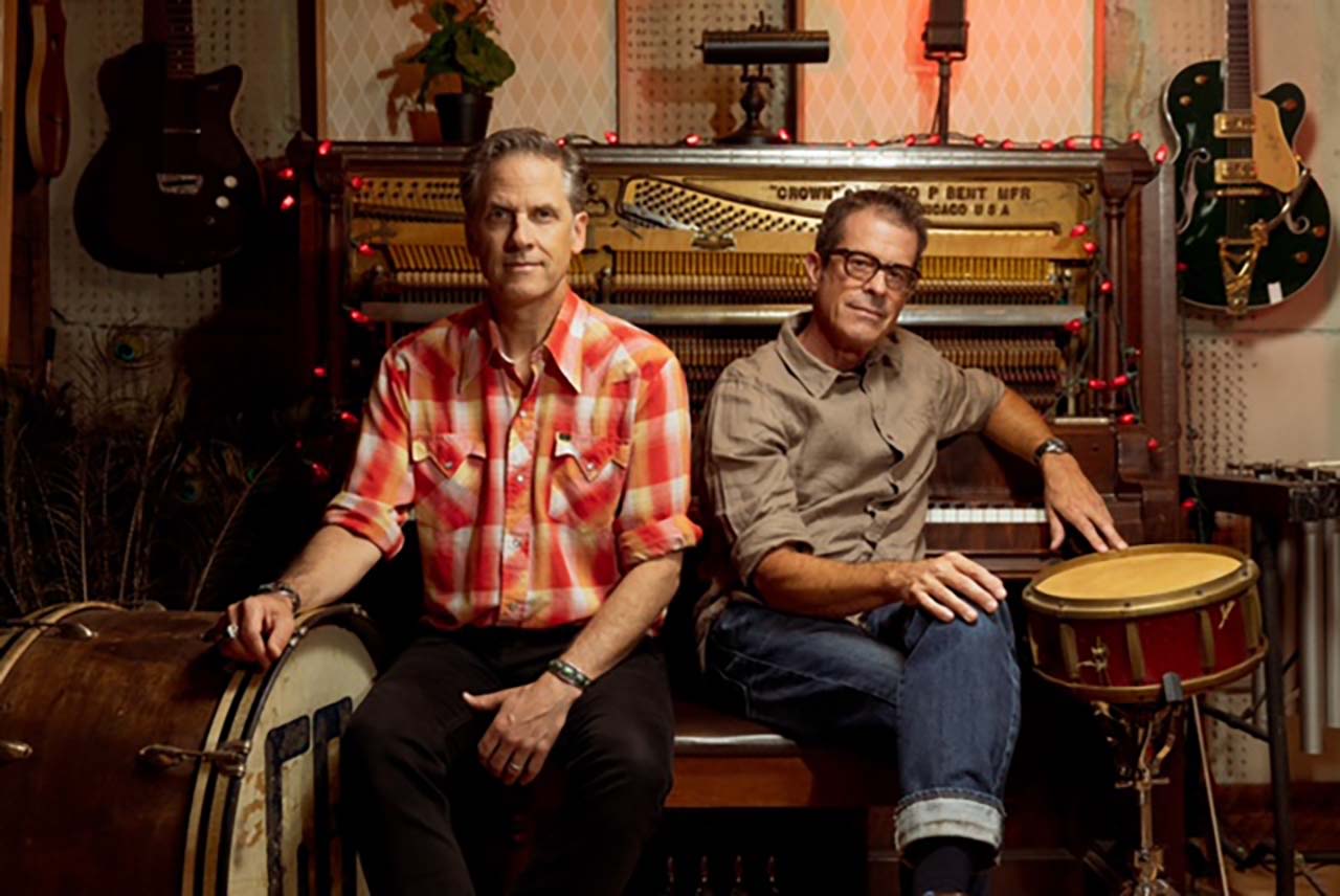 Calexico Americana duo Calexico sitting in front of a piano