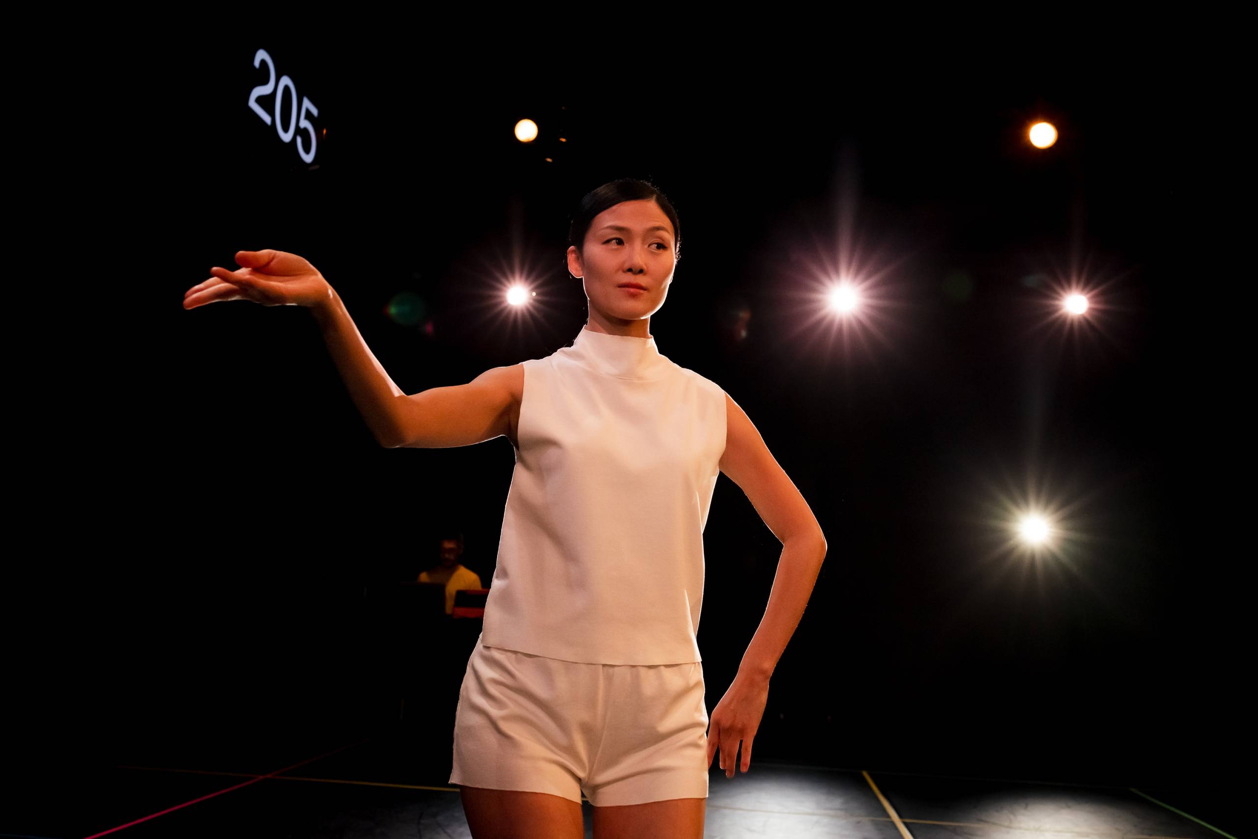 Woman in white performing on stage with bright lights and number 205 in the background.