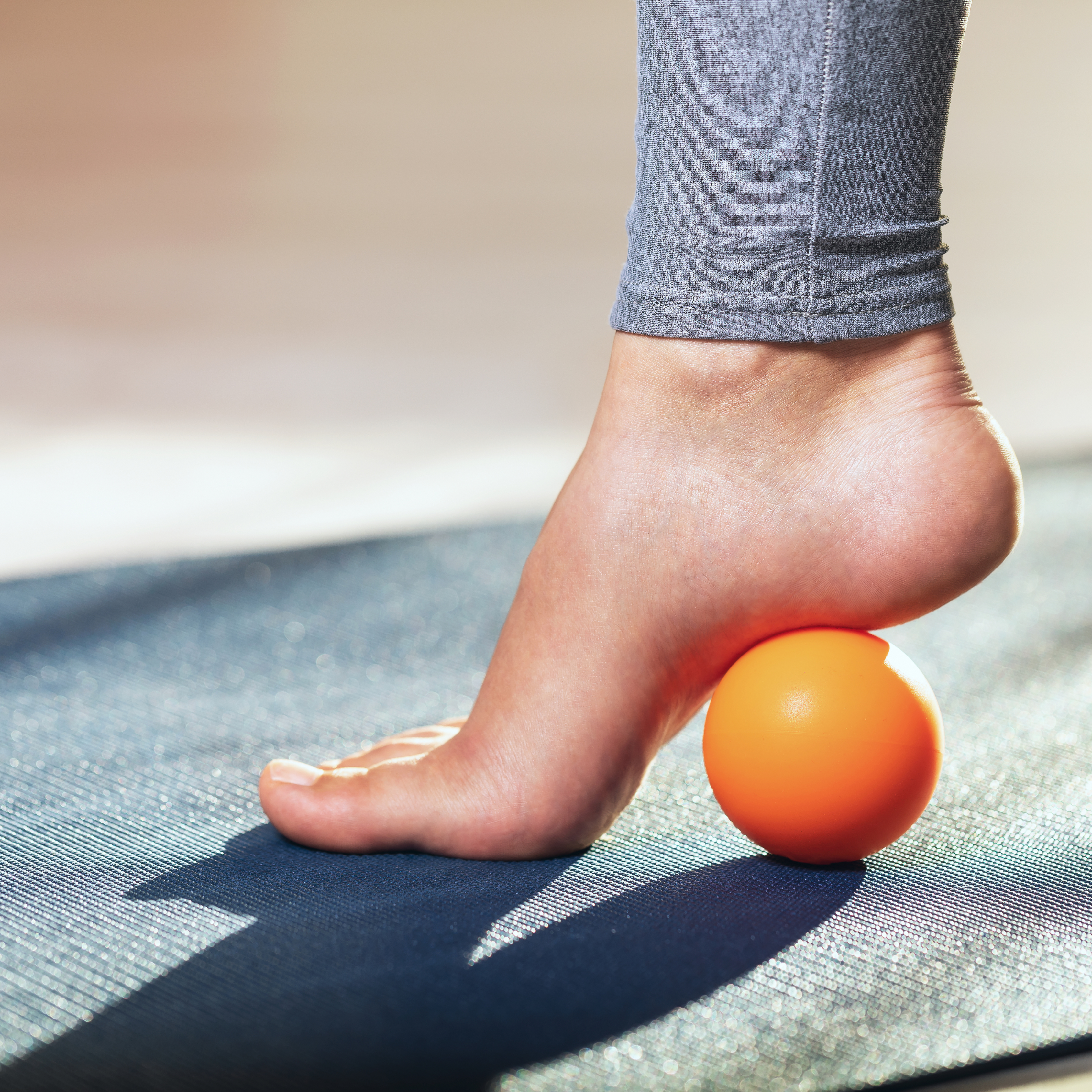 A woman's foot raised onto its toes, with an orange ball under the arch of the foot.