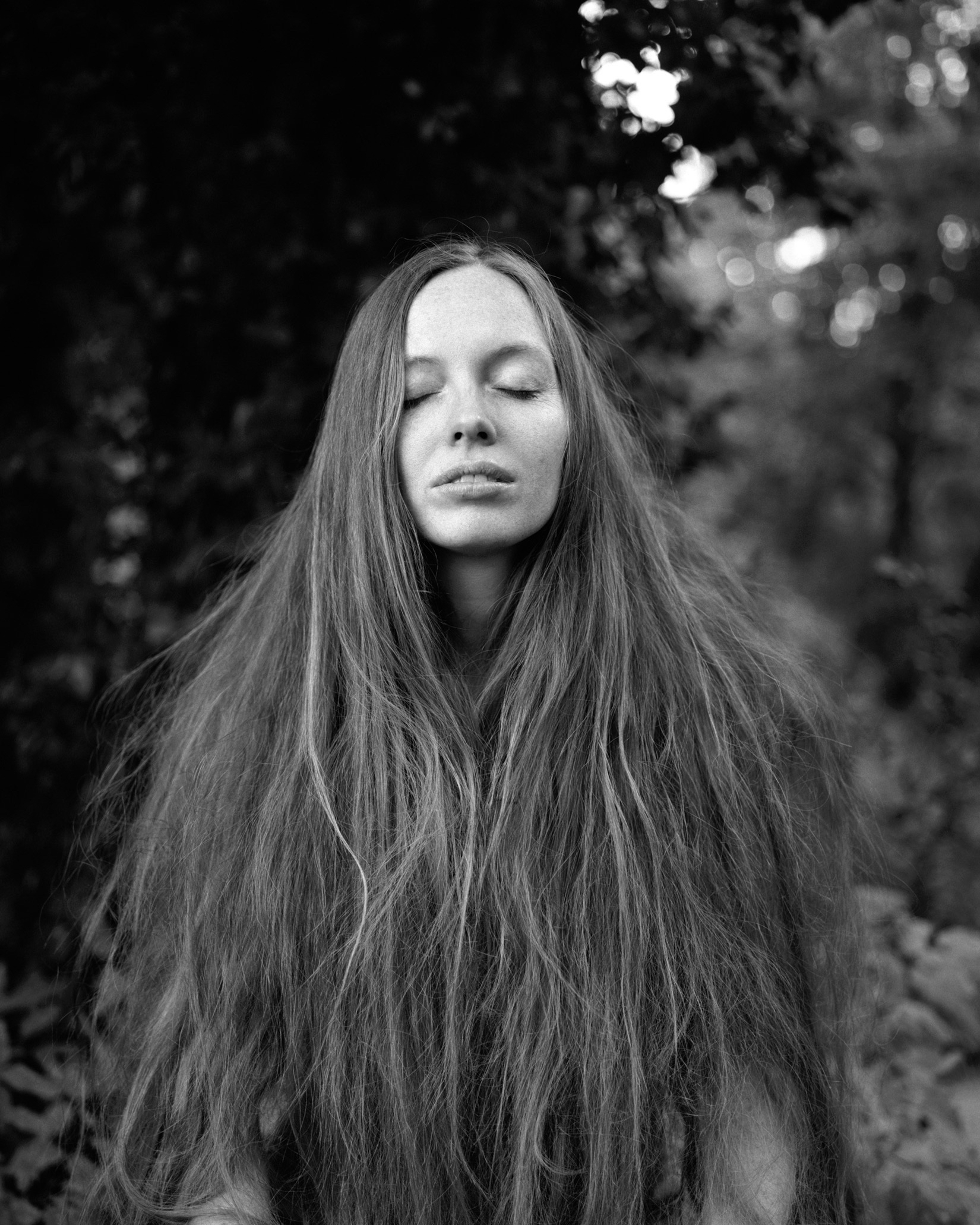 Fotografía en blanco y negro de una mujer con los ojos cerrados y su cabello largo hasta la cintura enmarcando su rostro