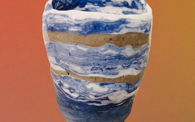 A handmade porcelain vase that was made with the Nerikomi method. The vase has a mixture of white and blue colors along with two brown tones striped across it.