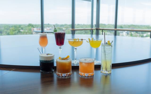 Row of cocktails in short glasses with another row of cocktails in tall glasses behind