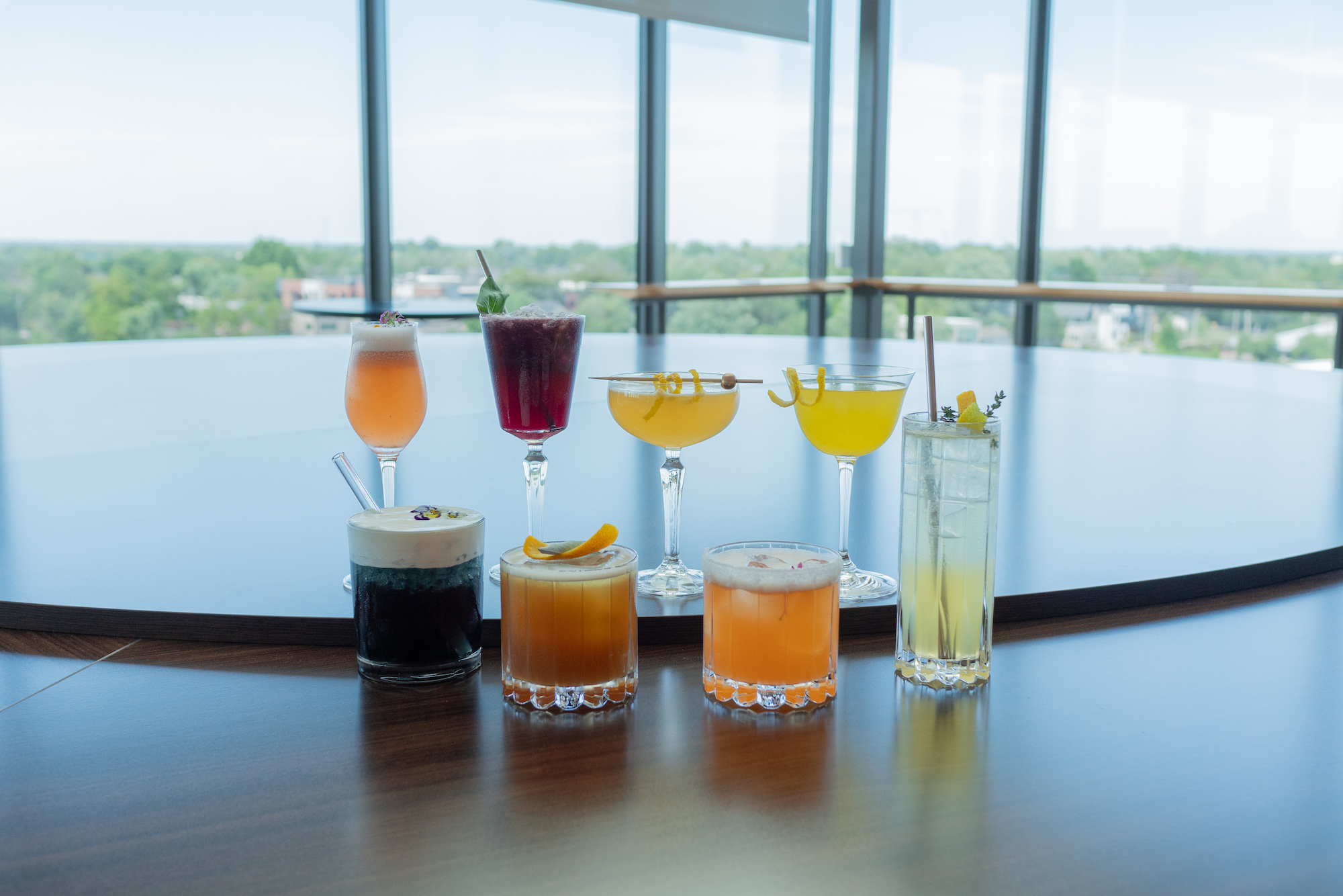 Row of cocktails in short glasses with another row of cocktails in tall glasses behind