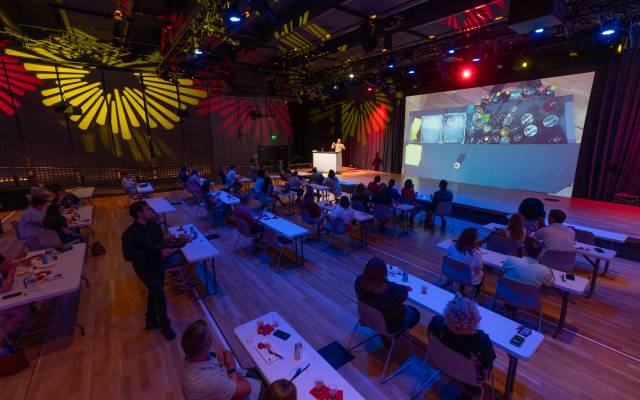 Audience at tables in colorfully lit room watching a presentation