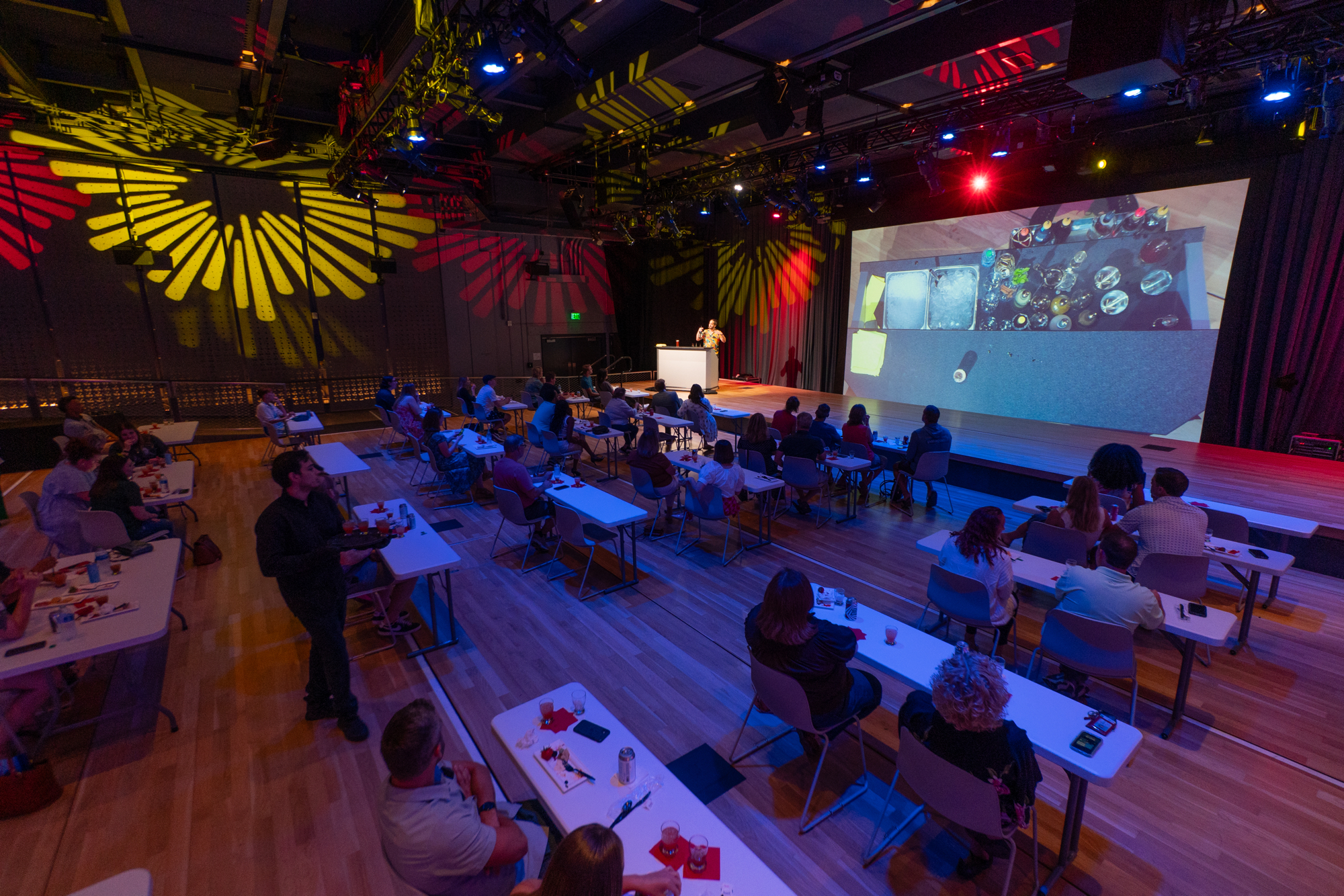 Audience at tables in colorfully lit room watching a presentation