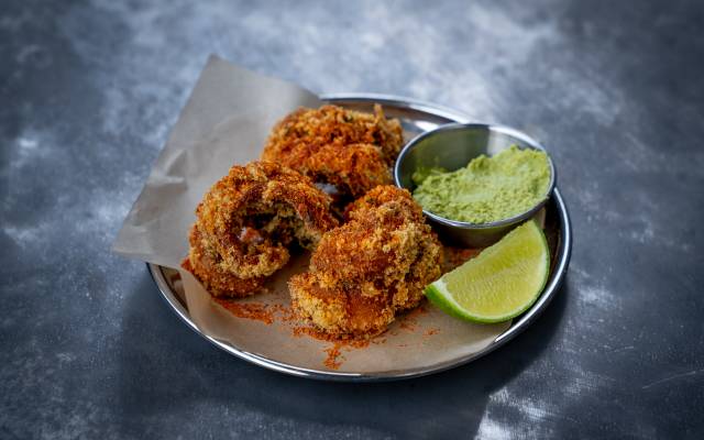 A small plate with the Bombil Fry dish garnished with limes and a red sauce drizzled on top of the fried food.