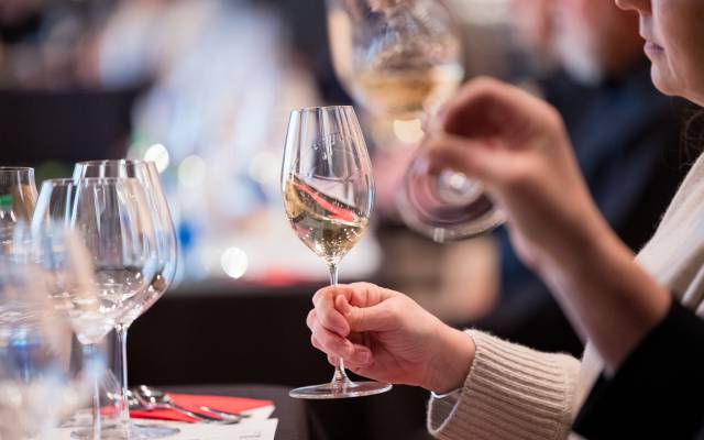 Person holding a wine glass at tasting, others are on the table in the background.