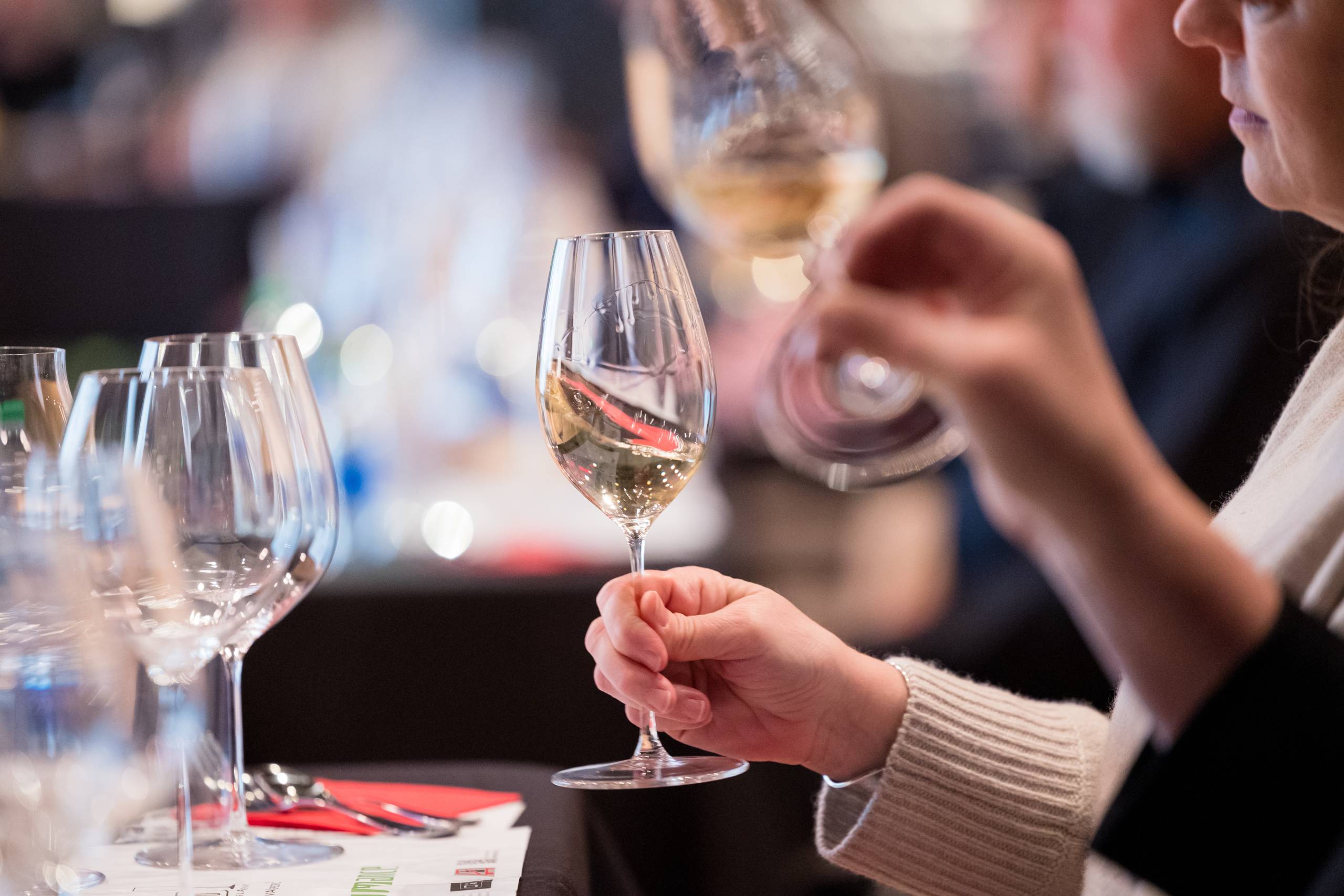 Person holding a wine glass at tasting, others are on the table in the background.