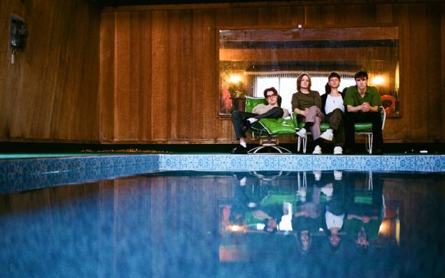 A group photo of the band Hippo Campus with a swimming pool in the foreground