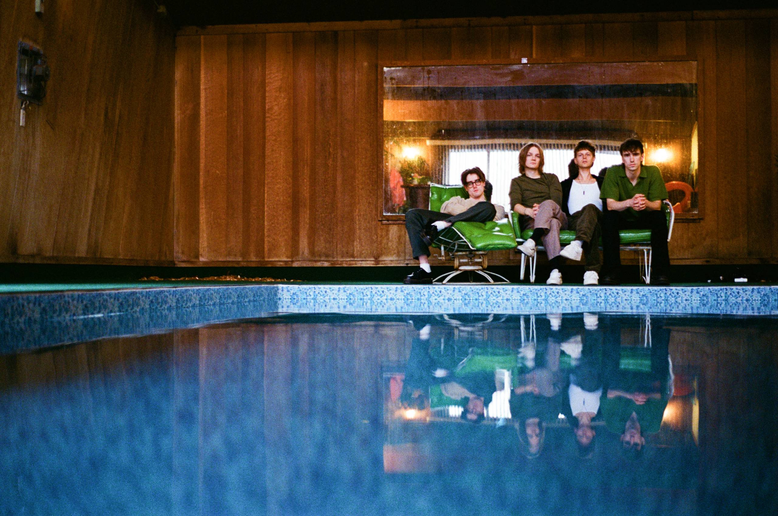 A group photo of the band Hippo Campus with a swimming pool in the foreground