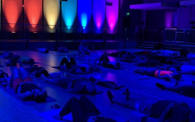 People lying on mats in a dim room with vibrant blue and purple ambient lighting.