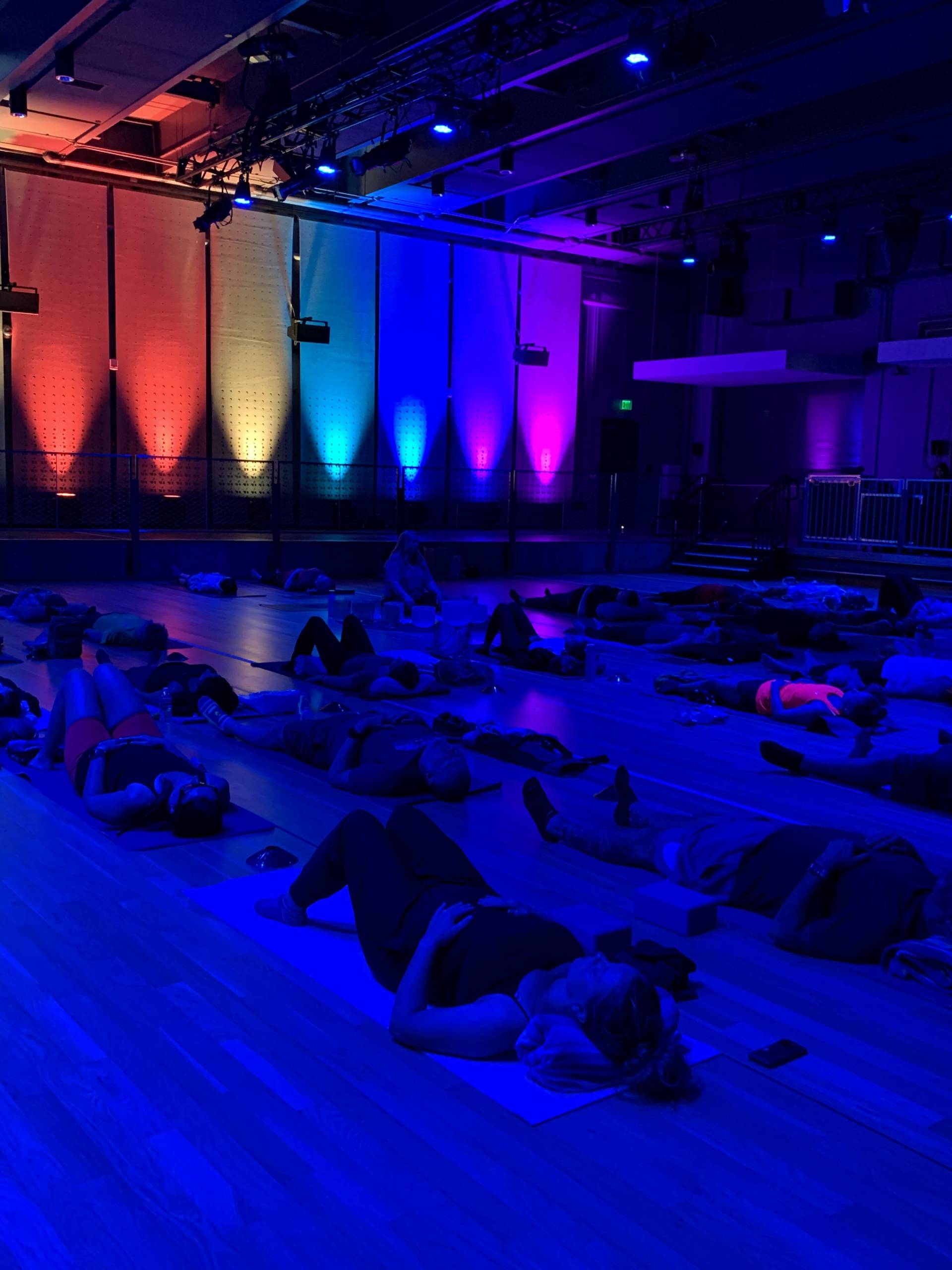 People lying on mats in a dim room with vibrant blue and purple ambient lighting.