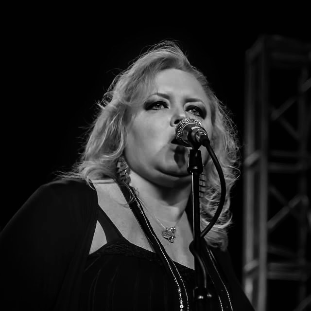 dawn cate trio Woman with light hair sings on stage in dark attire, metal stage setup in black and white.