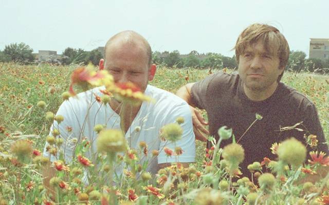 People sitting among wildflowers under clear sky with buildings in distant background.