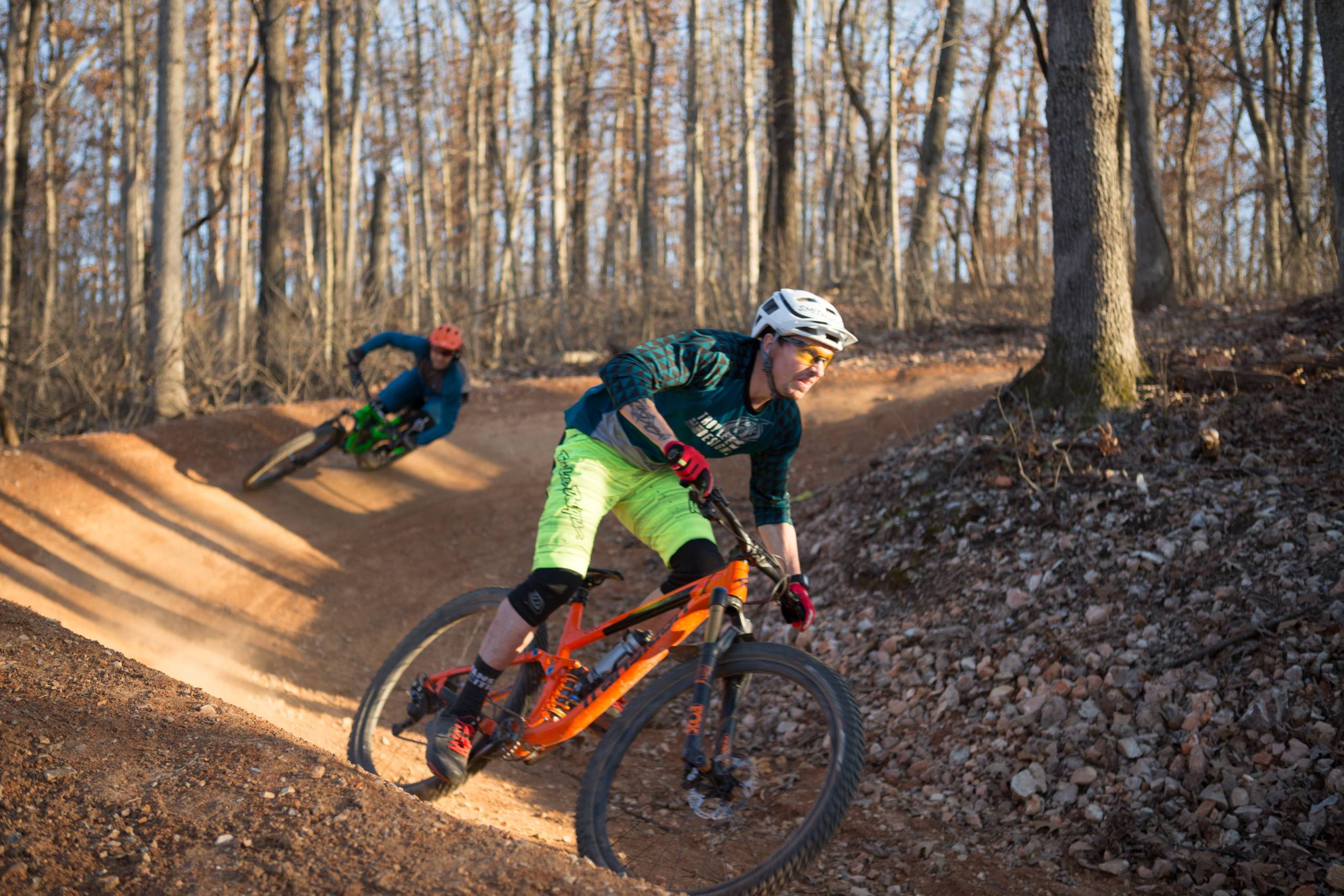 Two mountain bikers skillfully navigating a dirt trail in a forested area.