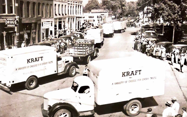 Historic parade with Kraft cheese trucks on a small-town street, lined with spectators.