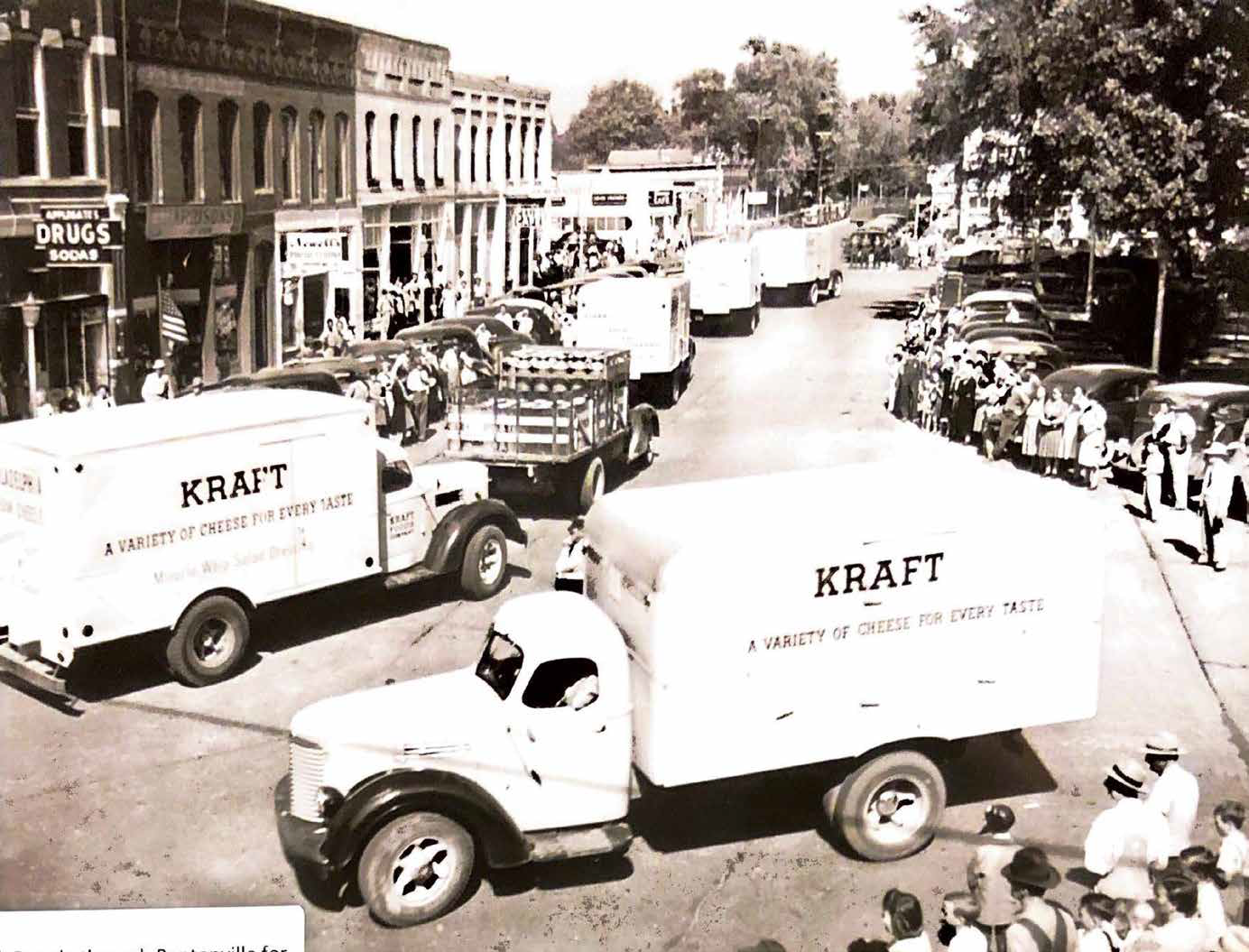 Historic parade with Kraft cheese trucks on a small-town street, lined with spectators.