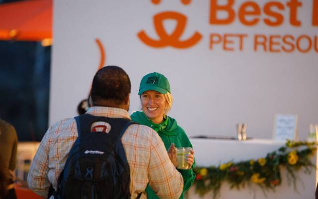 Woman in green cap and hoodie smiling, holding cup, with man at Best Friends Pet Resource Center.