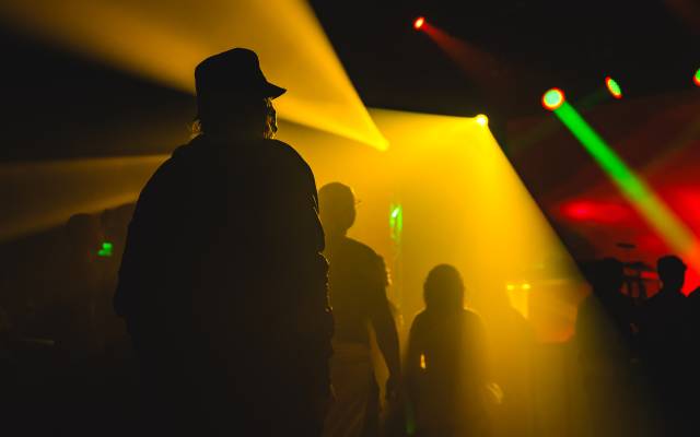 Silhouettes in dim venue with yellow and green stage lights creating a colorful atmosphere.
