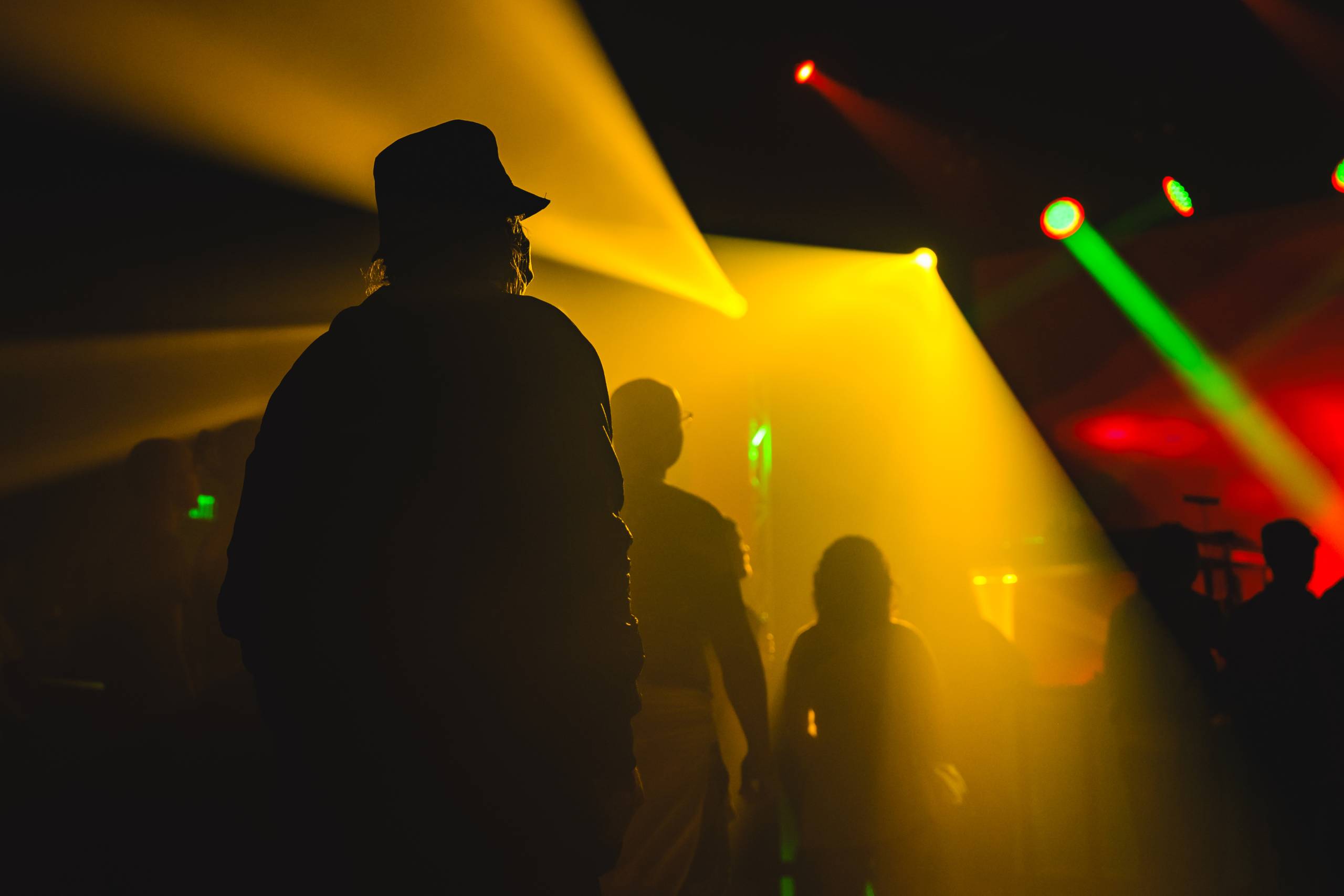 Crowd by Ismael Quintanilla III for Format 2023_DSC4379 Silhouettes in dim venue with yellow and green stage lights creating a colorful atmosphere.