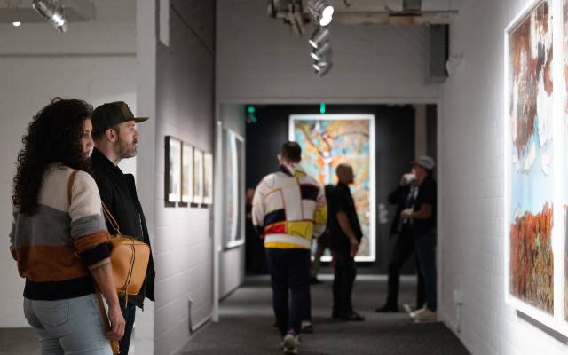 People in a modern art gallery, observing and discussing framed artworks on white brick walls.