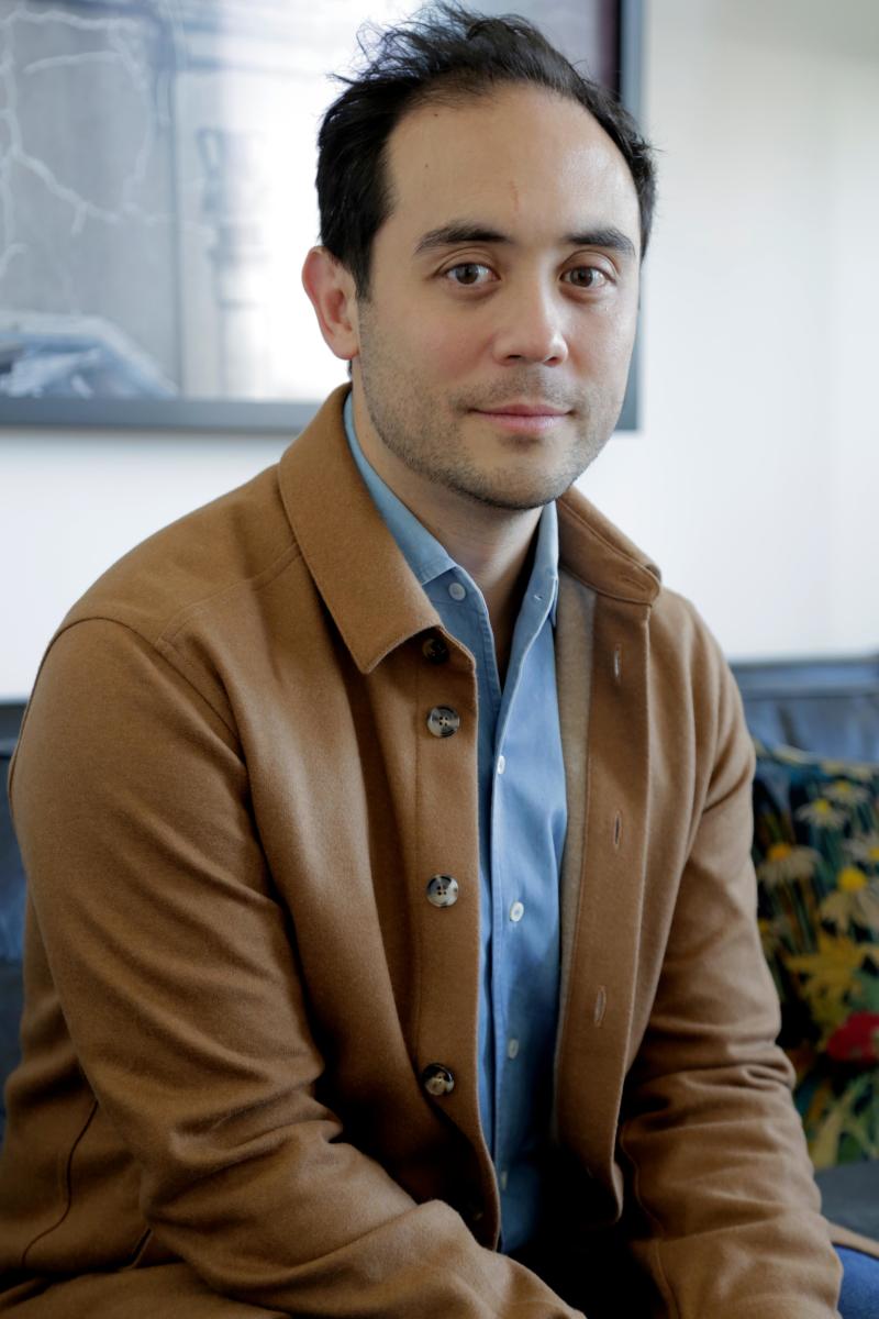 Man in brown jacket over blue shirt sitting indoors, framed picture background