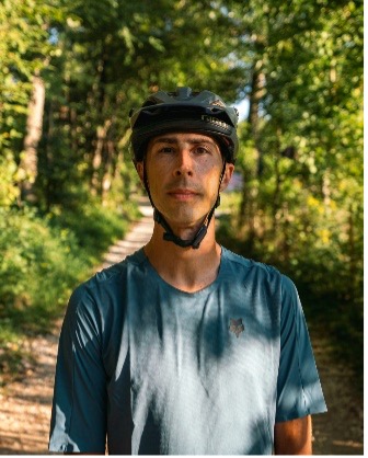 Person in helmet and blue shirt on a forest path with trees and sunlight in background.