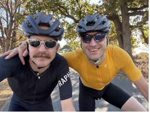 Two cyclists in helmets and sunglasses pose outdoors, one in black, the other in yellow.