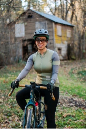 Person in cycling gear on a bike in woodland, rustic wooden building in background.