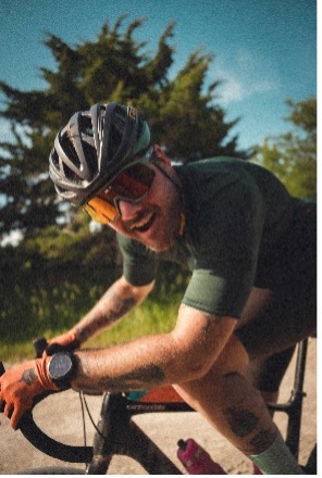 Cyclist wearing a helmet and sunglasses riding outdoors with trees and blue sky in the background.